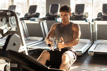 Muscular man exercising in gym, training hard and pulling weights in seated cable row machine....