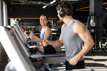 Young man and woman enjoying cardio workout in modern gym interior, running on treadmills, looking...