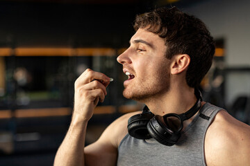 Sportive man taking supplement capsule, eating omega 3 or amino acid multivitamin pill, gym interior