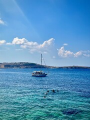 Obraz premium seascape of the island of Malta with a view of a sailboat on the turquoise-colored Mediterranean Sea with a rocky coast in the background on a sunny summer day 