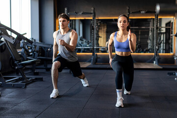 Personal training for two. Fitness man and woman do lunges exercises to warm up and burn leg muscles, modern gym interior