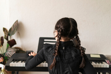 Little girl playing the piano at home. The child learns to play the keyboard.