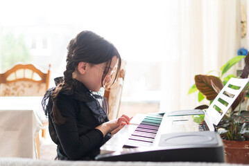 Cute little girl playing piano at home. Early education concept.
