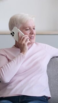 Cheerful senior Caucasian woman using smartphone for talking at home. Remote communication and happy retirement concept. Vertical video.