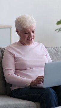 Senior Caucasian cheerful woman remote working with laptop at home. Distant online work, digital entertainment and communication concept. Vertical video.
