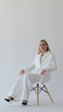 Serious portrait of a concentrated Caucasian female executive, businesswoman, chief, boss or CEO sitting on chair on white background. Vertical video.