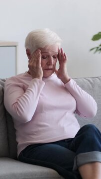 Exhausted elderly Caucasian woman suffering from migraine at home. Tension and high blood pressure. Age related disease concept. Vertical video.