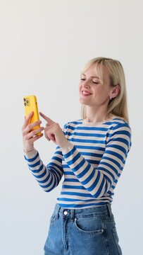 Happy Caucasian woman using smartphone for messaging in social media or browsing internet on white background. Online entertainment concept. Vertical video.