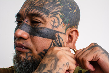An asian man with extensive face tattoos fixes or puts on his flesh tunnel or large plug into his...