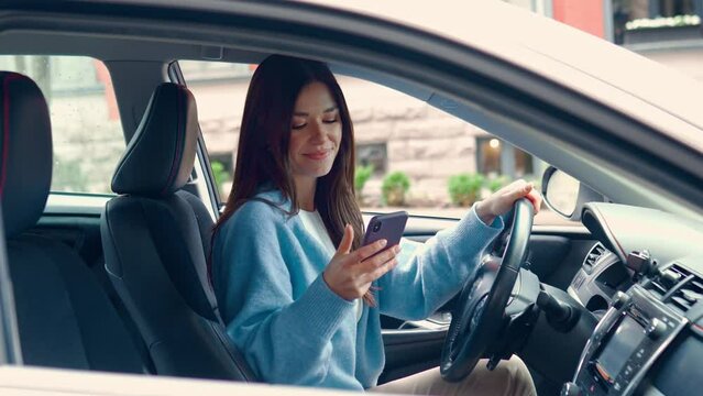 Young happy woman driver sitting inside car holding smartphone using gps navigation map app on mobile phone looking at cellphone chacking traffic on city roads. Driving applications concept.