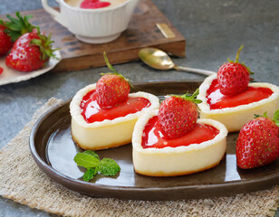 Close-up of heart shaped mini tart with vanilla cream and fresh strawberries on a tray on table