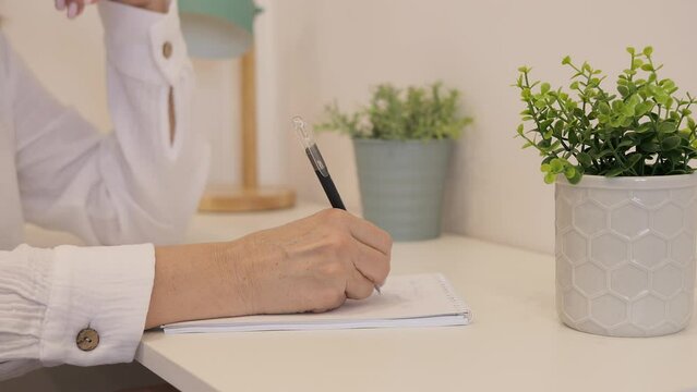 A woman diligently fills out diary on her desk. Her hand seems to dance, reflecting her thoughts on the pages of the diary. Attentively, she continues to write in her diary, noting important moments.