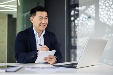 Smiling businessman with laptop and documents in office