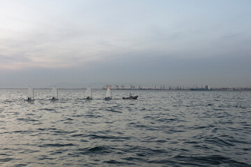 Choppy sea waters under a twilight sky with silhouettes of boats and a distant, faint city skyline at dusk.
