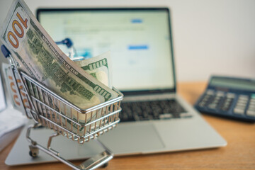 shopping cart full of 100 usd note bills and online shopping with laptop 