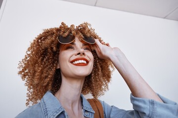 Joyful Expression: A Cheerful Young Woman with Curly Hair and Smiling Eyes, Wearing Goggles and Trendy Eyeglasses, Positively Enjoying a Funny Moment in Modern Fashion and Stylish Coiffure