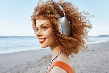 Summer Beach Vacation: Smiling Woman Embracing Freedom of the Sea amidst Nature's Emotion with Curly Hair and Freckles, Enjoying Happiness with Headphones in Outdoors.