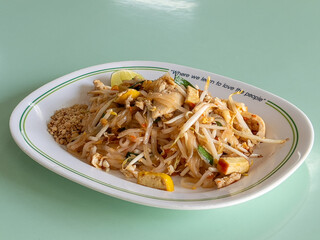 A plate of delicious Pad Thai with chicken, tofu, bean sprouts, and peanuts, garnished with a lime wedge.