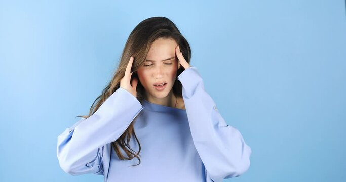 Attractive woman close up with strong headache. Beautiful young brunette touching her temples feeling stress or pain. Stress or headache concept. Negative human emotion isolated on blue background.