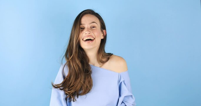 Optimistic brunette hair woman makes thumbs up gives approval shows excellent gesture says nice job gives positive feedback shares good opinion, wow, wear blue top isolated over blue background.
