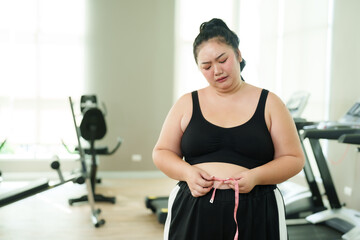 Overweight Asian woman exercise in gym, Pensive measuring waistline, reflecting on fitness journey,...