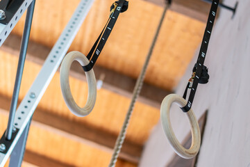 A pair of wooden rings hung from a bar with a black cord. Horizontal