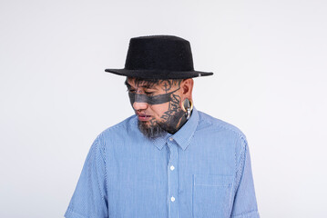 Portrait of a stylish Asian man featuring bold face tattoos, eye tattoo, and multiple body piercings, posing against a plain white background.