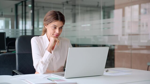 Busy mature middle aged professional business woman manager executive looking at laptop working on computer in office thinking of digital market plan or considering new corporate idea sitting at desk.