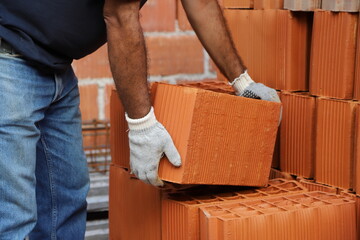 Builder working on construction site. Concept of architecture, construction, industry, construction worker.  Professional bricklayer working on house construction. Construction worker lifting a brick.