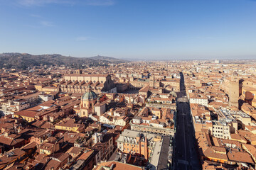 A panoramic view of Bologna historic city center from above. The red-tiled rooftops and cathedral domes create a picturesque scene, with hills on the horizon