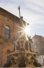 Sunrays pierce through the silhouette of Neptune Fountain in Bologna, casting a dazzling effect on...