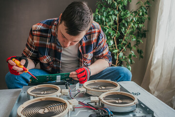 Focused man repairs the electronic components of a stove cooktop, tools in hand, in a home setting with natural light filtering through. Repairman repairs household appliances in the apartment.
