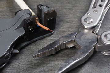 Wire stripper and electrical cable on gray workbench background close up.