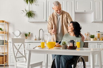 A man stands next to his wife in a wheelchair in their home kitchen.