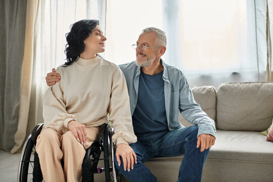 A disabled woman in a wheelchair engages in conversation with a man in the living room.