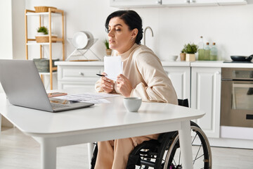 A disabled woman in a wheelchair working remotely on her laptop from her kitchen.