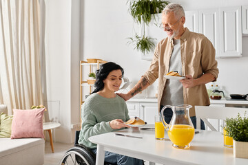 A man in a wheelchair serves food to a woman in a wheelchair in their home kitchen, symbolizing...