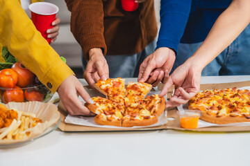 .Young Asian students gather with friends for a pizza party, laughing and sharing slices. Enjoying...