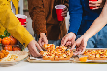 .Young Asian students gather with friends for a pizza party, laughing and sharing slices. Enjoying fast food delivery, they embody diversity and togetherness in a relaxed, enjoyable lifestyle.