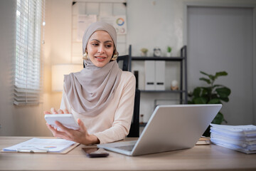 Young Muslim businesswoman holds a meeting over the phone and calculates company finances on her...