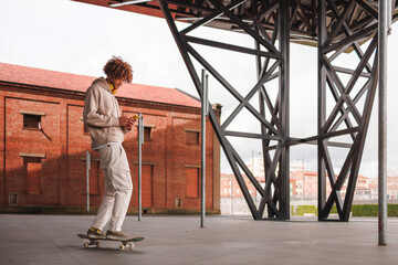Young guy with curly hair skateboarding and using cellphone.