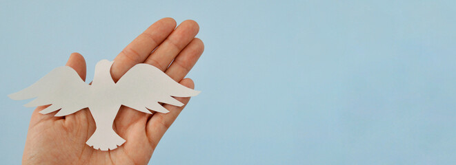 White paper origami bird on blue background. World Day of Peace. Day Against Humiliation. International Day Of Human Fraternity. International Day of Living Together in Peace. Banner