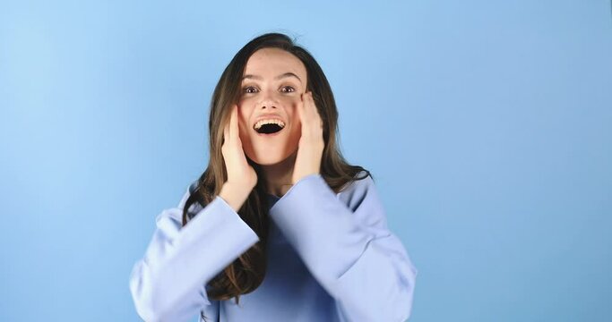 Happy woman looking camera shocked surprised say wow cover mouth spread hands. Wow, it is awesome. Surprised girl face. Close up of shocked woman face expression isolated on blue background. Blow mind