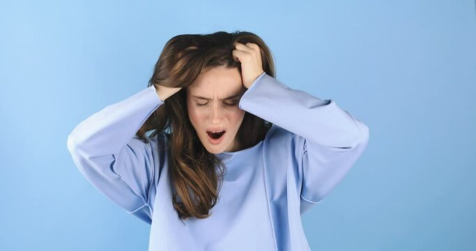 Frustrated nervous woman mad touching head against blue background. Annoyed irritated young woman with an angry face looking furious, mad and feeling frustrated. Unhappy lose.
