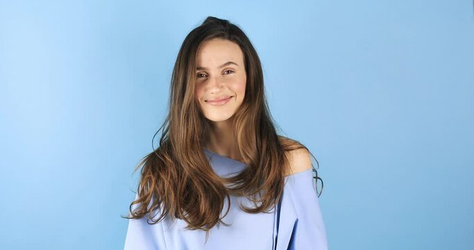Gorgeous sensual slim tender Caucasian woman in blue pullover shake head, care cosmetics products brunette hair. Girl waving fluttering hair shaking head and fix hair isolated on blue background.