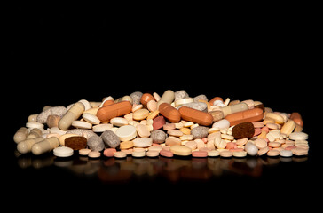 A pile of different medicine tablets on a black background. A group of medicine pills