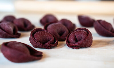 Beetroot tortelli poised for the pot, a medley of ricotta and cheese. Italian culinary craft in close-up, gourmet pasta ready to enchant the palate. Italian cuisine product. - obrazy, fototapety, plakaty