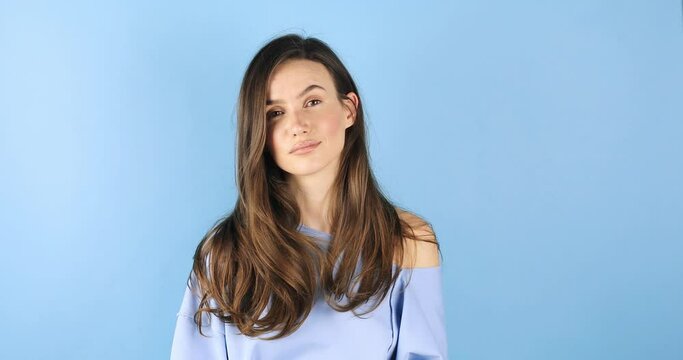 Smiling attractive brunette woman looking at camera listening to someone and nodding with agree standing over blue studio background. Girl wave her head.