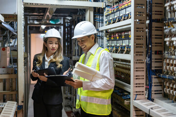 Happy Asian male and female engineers working in power plant, discussing projects, wearing hard...