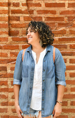Mujer adulta con cabello rizado sonriendo frente a una pared de ladrillo. Chica Guatemalteca bonita.